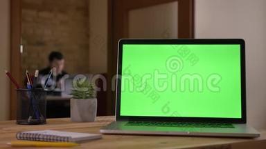 笔记本电脑绿色屏幕的特写镜头放在笔记本旁边的桌子上，铅笔放在一个杯子里，上面显示着一个